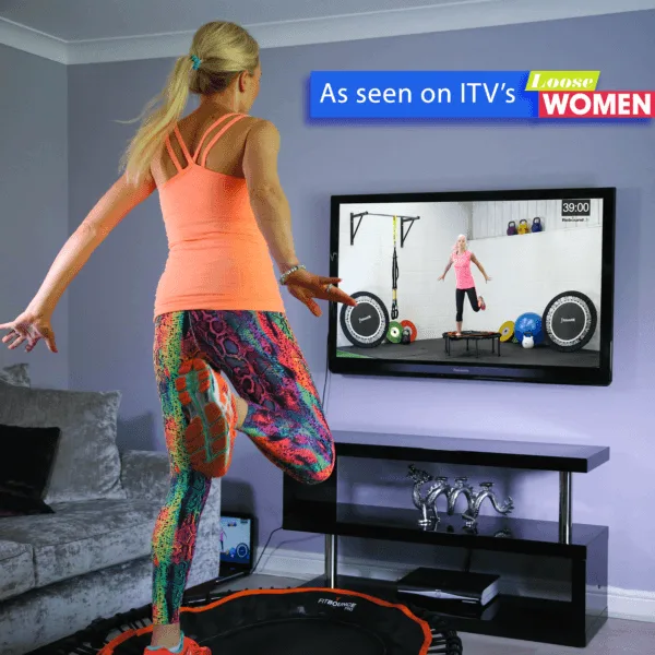 Woman bouncing in living room on fit bounce pro rebounder watching online workout on TV from Rebound Fitness
