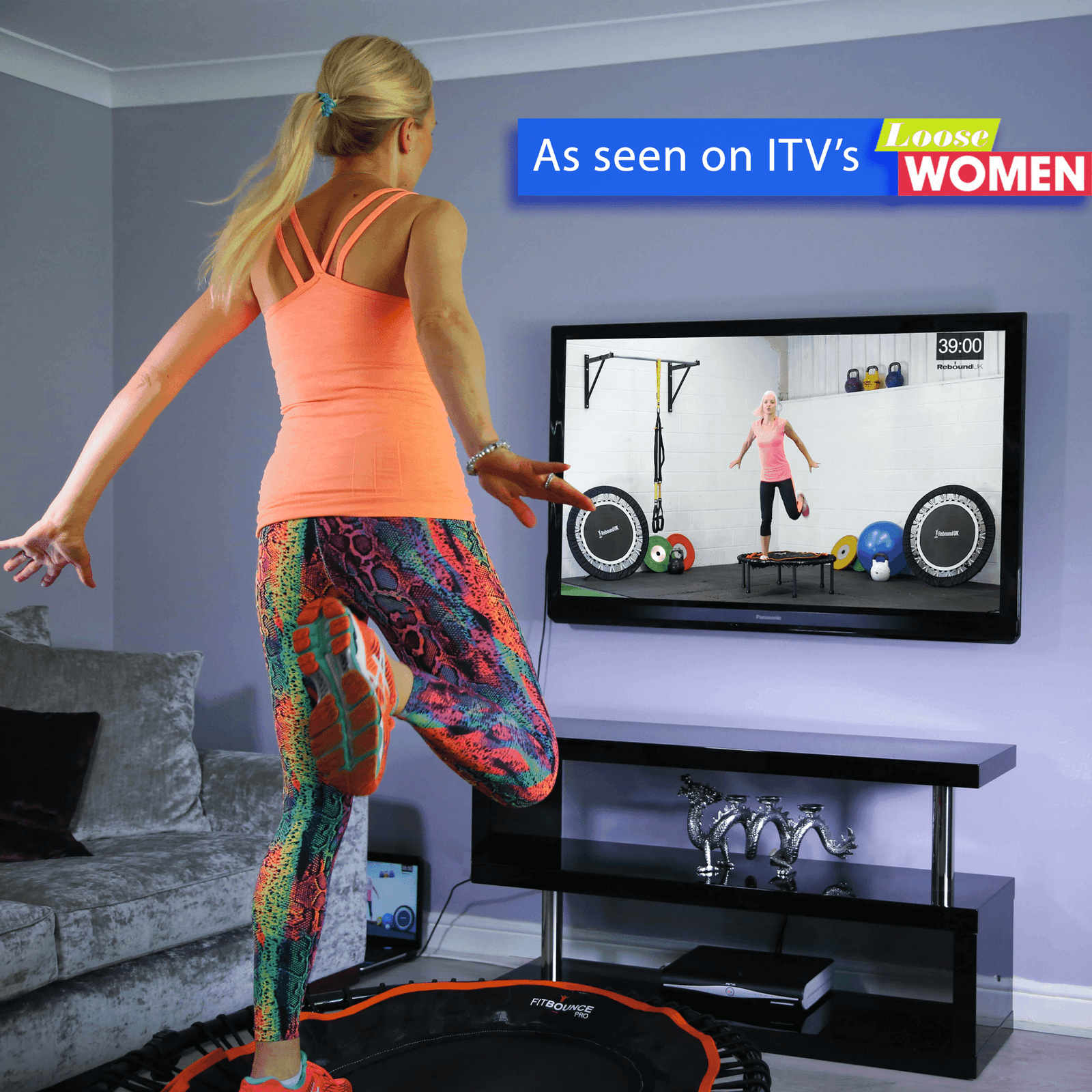 Woman bouncing in living room on fit bounce pro rebounder watching online workout on TV from Rebound Fitness